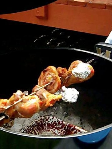 Turkey legs on a rotisserie spit in a kettle grill