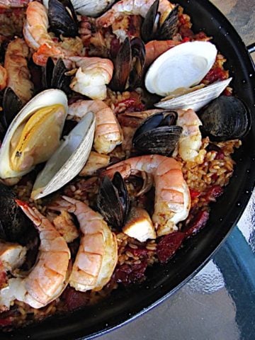 Pan full of cooked paella, covered with clams, mussels, and shrimp, on a glass table