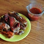 A plate of cooked western shoulder ribs with a measuring cup full of BBQ sauce