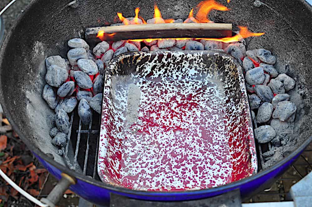 Charcoal grill setup - drip pan in the middle, coals in a U shape towards the legs, smoking wood in the back.