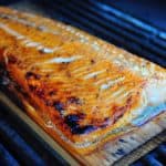 A cooked filet of salmon on a cedar plank on a grill
