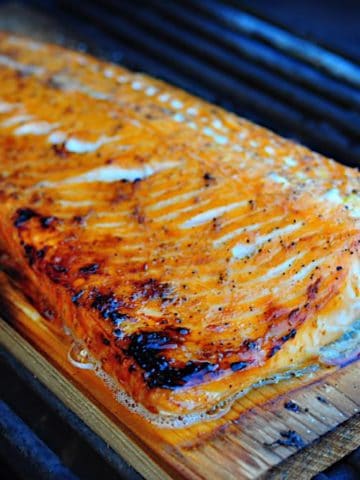 A cooked filet of salmon on a cedar plank on a grill