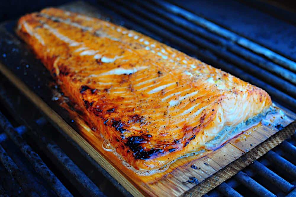 A cooked filet of salmon on a cedar plank on a grill