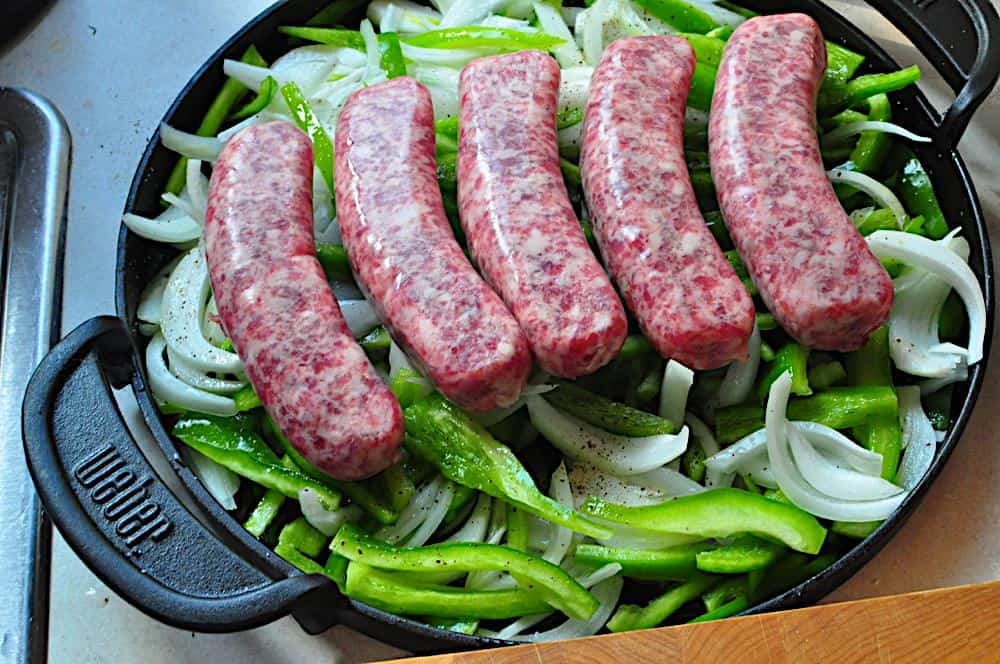 Pan with brats on top of sliced peppers and onions