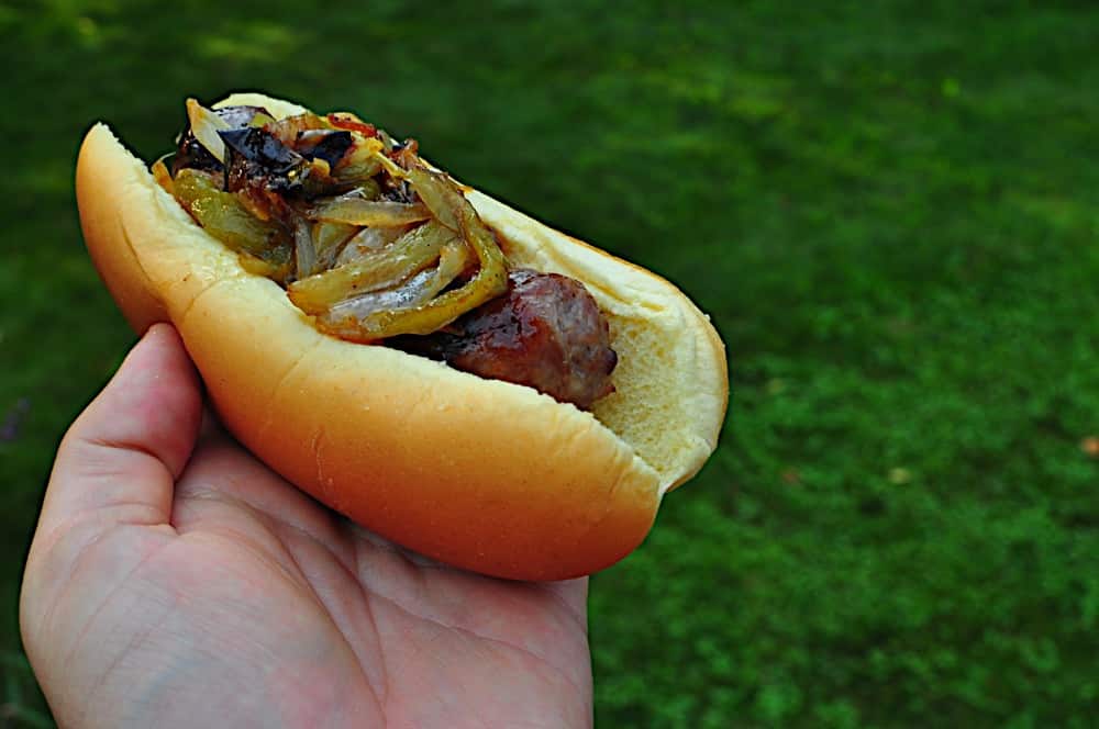 A cooked brat with peppers and onions