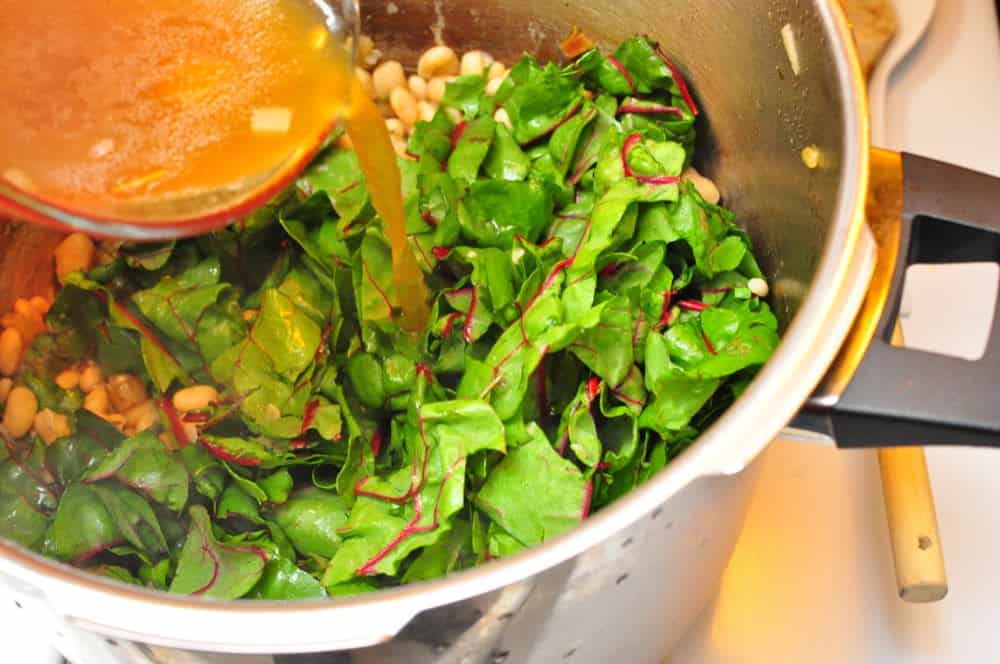 Pouring bean broth over the chopped chard leaves and beans in the pressure cooker