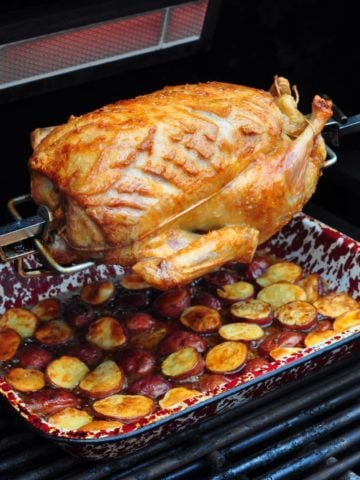 Duck on a gas grill rotisserie with drip pan potatoes