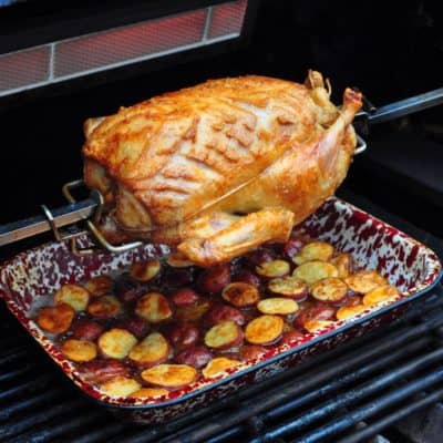 Duck on a gas grill rotisserie with drip pan potatoes