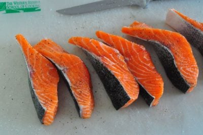 Salmon filets on a cutting board, sprinkled with salt and pepper