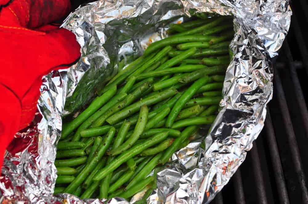 A gloved hand opening a foil pouch of green beans
