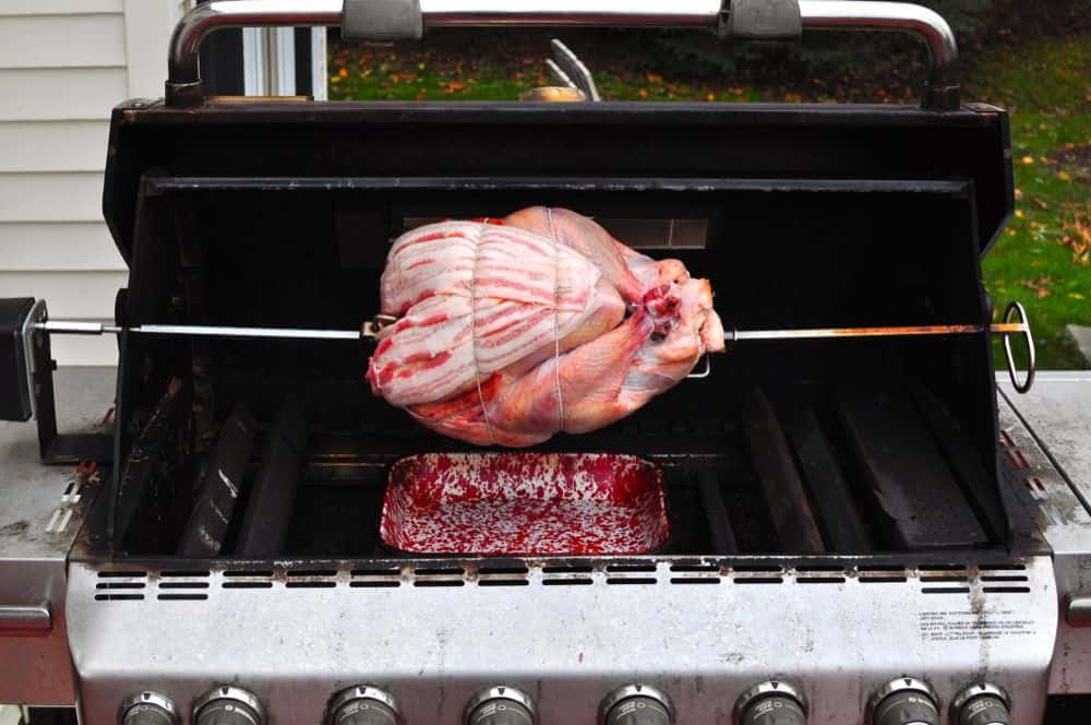 Turkey ready to rotisserie grill in a gas grill - on the spit with a drip pan underneath.