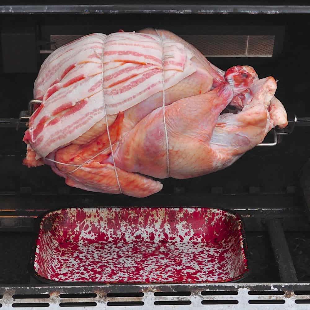 A turkey with bacon tied to the breast, in a grill, on a rotisserie spit