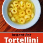 A white bowl of tortellini in broth, on a wooden table