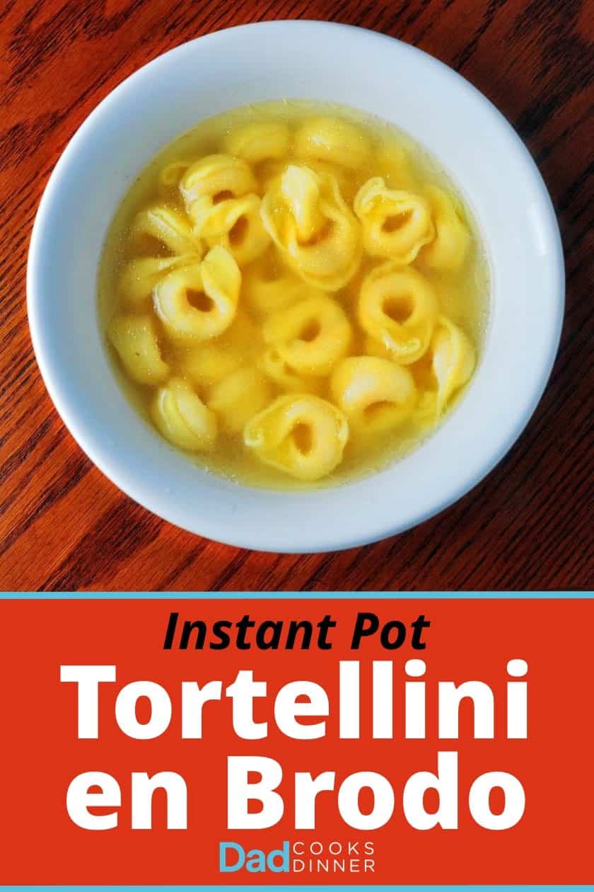 A white bowl of tortellini in broth, on a wooden table