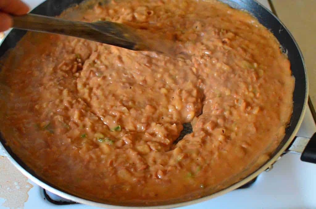 A frypan of thickened refried beans, with a wooden spoon