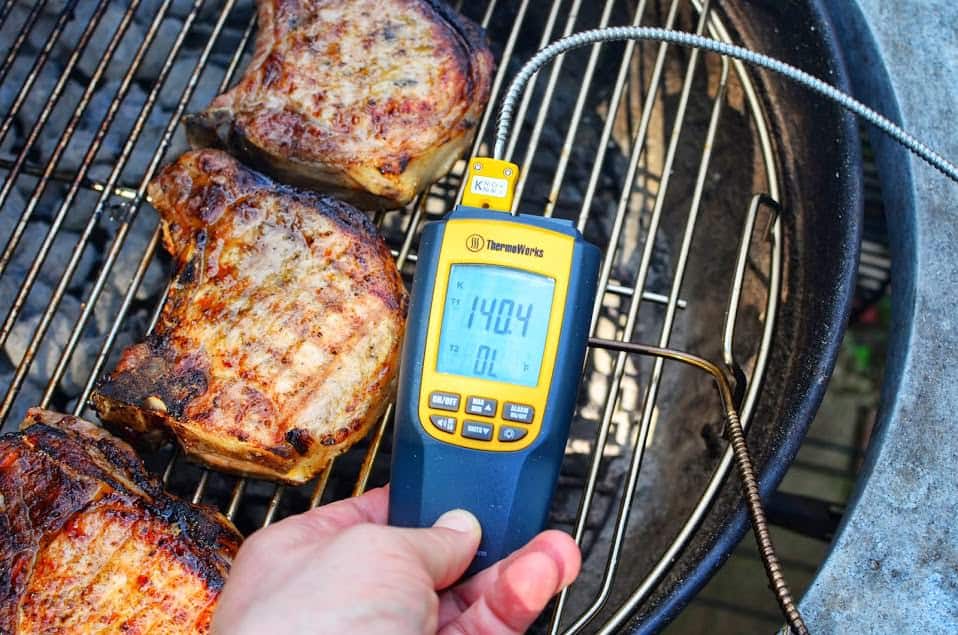 Checking the temperature of pork chops on the grill with a probe thermometer