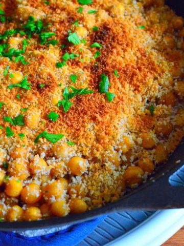 A frypan full of chickpeas, topped with a toasted bread crumb crust and a few parsley leaves