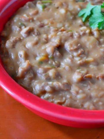 A red bowl of refried pinto beans, with a few cilantro leaves on top