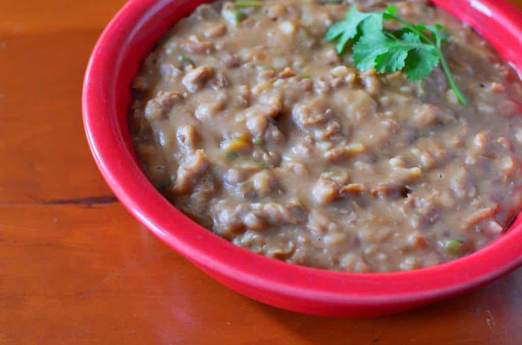 A red bowl of refried pinto beans, with a few cilantro leaves on top
