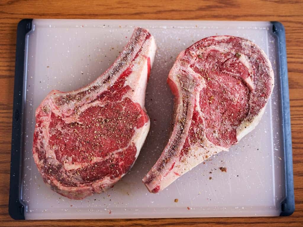 Ribeye steaks salted on a plastic cutting board