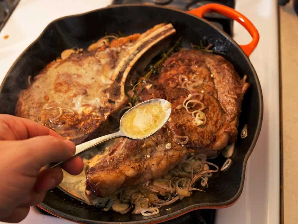 Spooning butter over ribeye steaks in a cast iron skillet