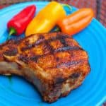 Grilled bone-in pork chop sprinkled with a spice rub on a blue plate with multicolored mini-peppers