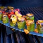 Jalapeno peppers stuffed with melted cheese in a rack on a grill