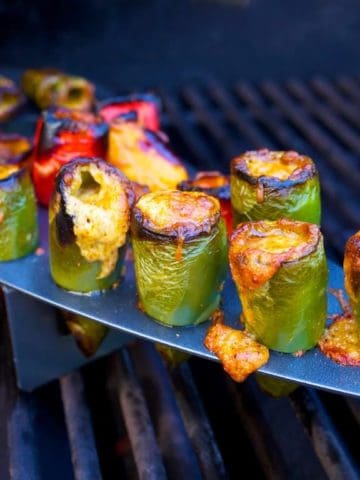 Jalapeno peppers stuffed with melted cheese in a rack on a grill