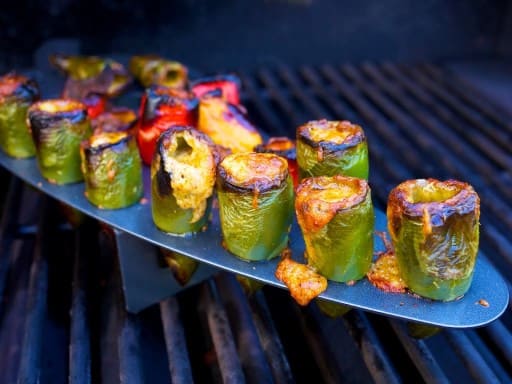 Jalapeno peppers stuffed with melted cheese in a rack on a grill