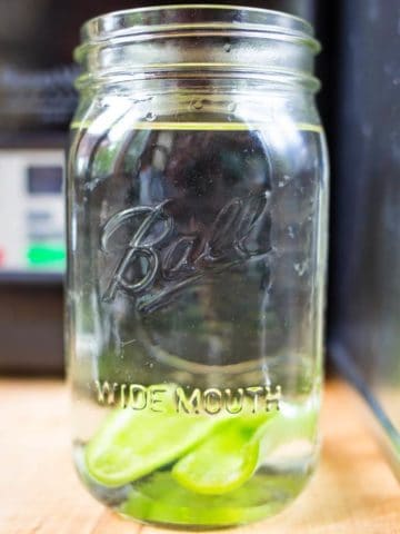 Canning jar full of tequila with sliced jalapeno pepper wedges sunk to the bottom