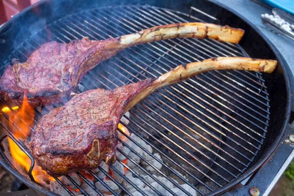 A pair of tomahawk steaks searing on a kettle grill