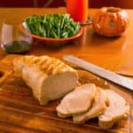 A sliced pork loin roast on a cutting board with a carving knife, green beans, a candle, and a pumpkin in the background