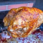 A turkey breast on a grill's rotisserie, with a lit rotisserie burner in the background.