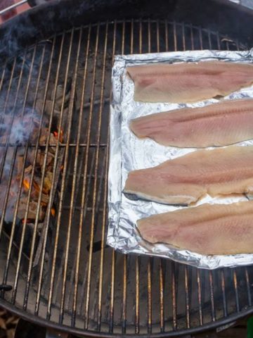 Grill Smoked Trout: trout on a foil sheet, on a grill, with smoking coals on the other side of the grill