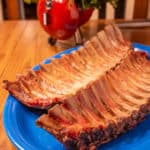 Two cooked slabs of ribs on a platter in front of a flower arrangement that looks like a kettle grill