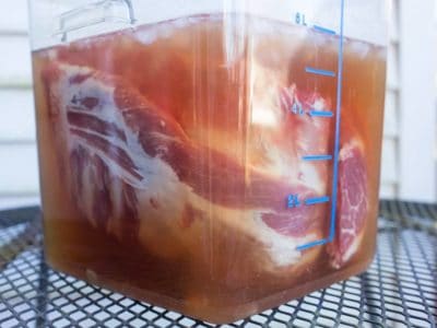 Baby back ribs floating in a brown-sugar and herb brine in a food storage container