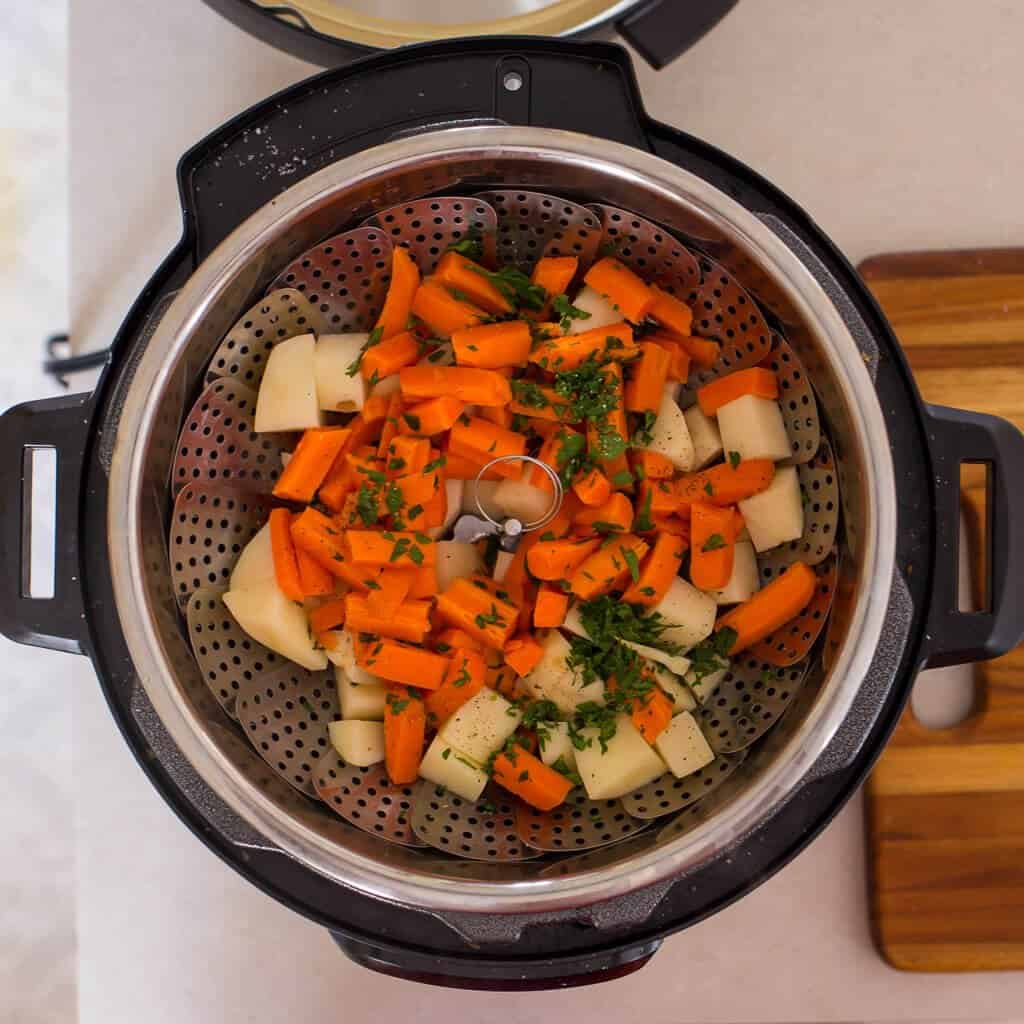 Instant Pot with a steamer basket of potatoes and carrots on top.