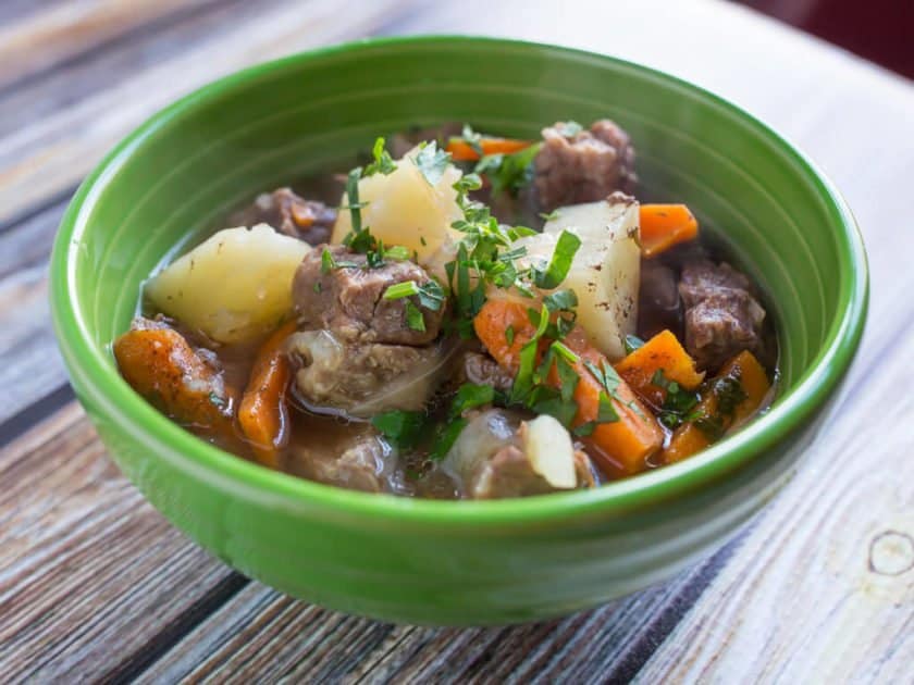 Side view of a green bowl full of stew, with chunks of potatoes, carrots, and lamb, sprinkled with parsley.