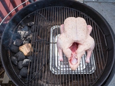 Kettle grill with lit coals on the left and a duck over a drip pan on the right
