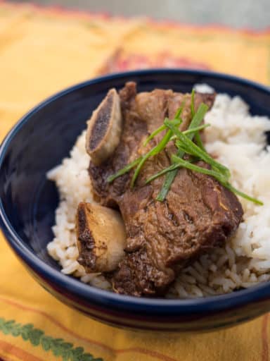 Braised short ribs on rice in a blue bowl, sprinkled with slivered scallions