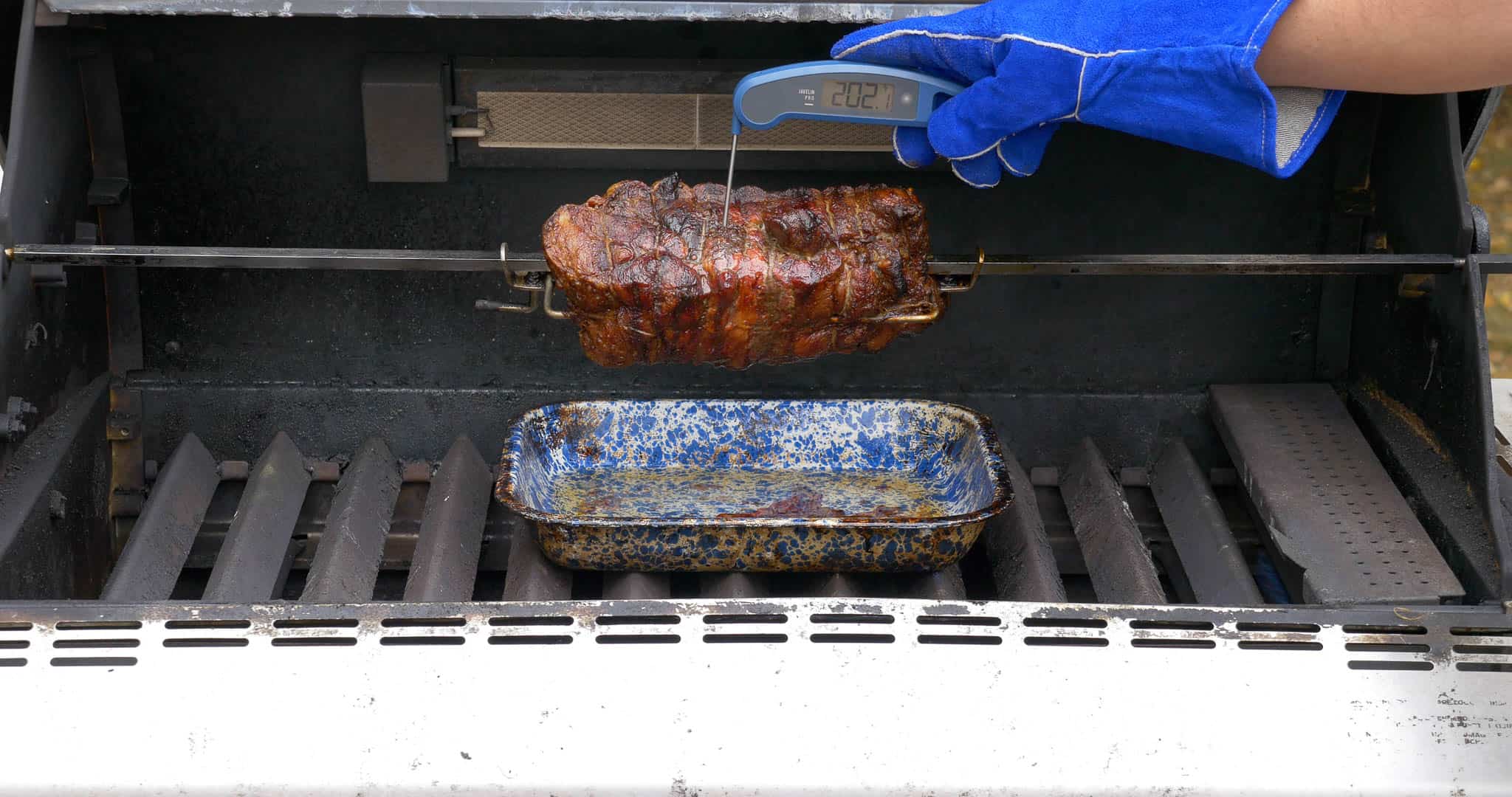 Checking the temperature of a rotisserie pork shoulder with an instant read thermometer