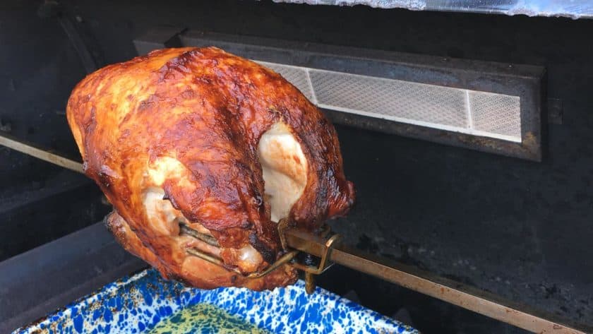 Browned rotisserie turkey breast in a grill, on a spit, over a speckled blue drip pan
