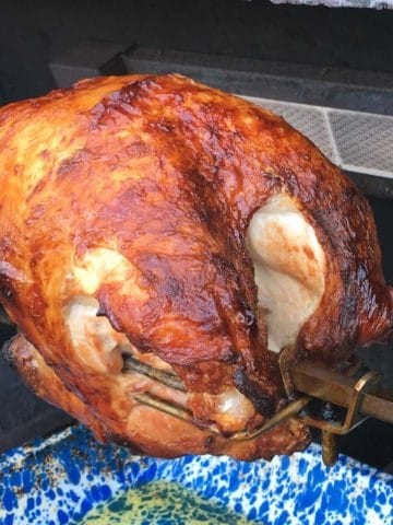 Rotisserie turkey breast on a spit in a grill above a blue speckled drip pan