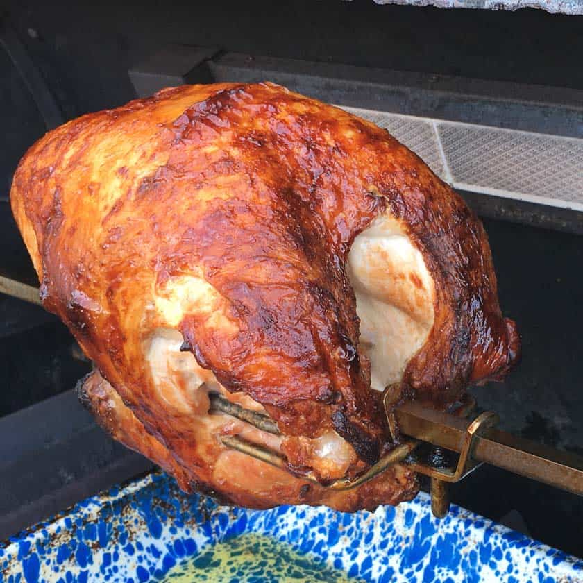 Rotisserie turkey breast on a spit in a grill above a blue speckled drip pan