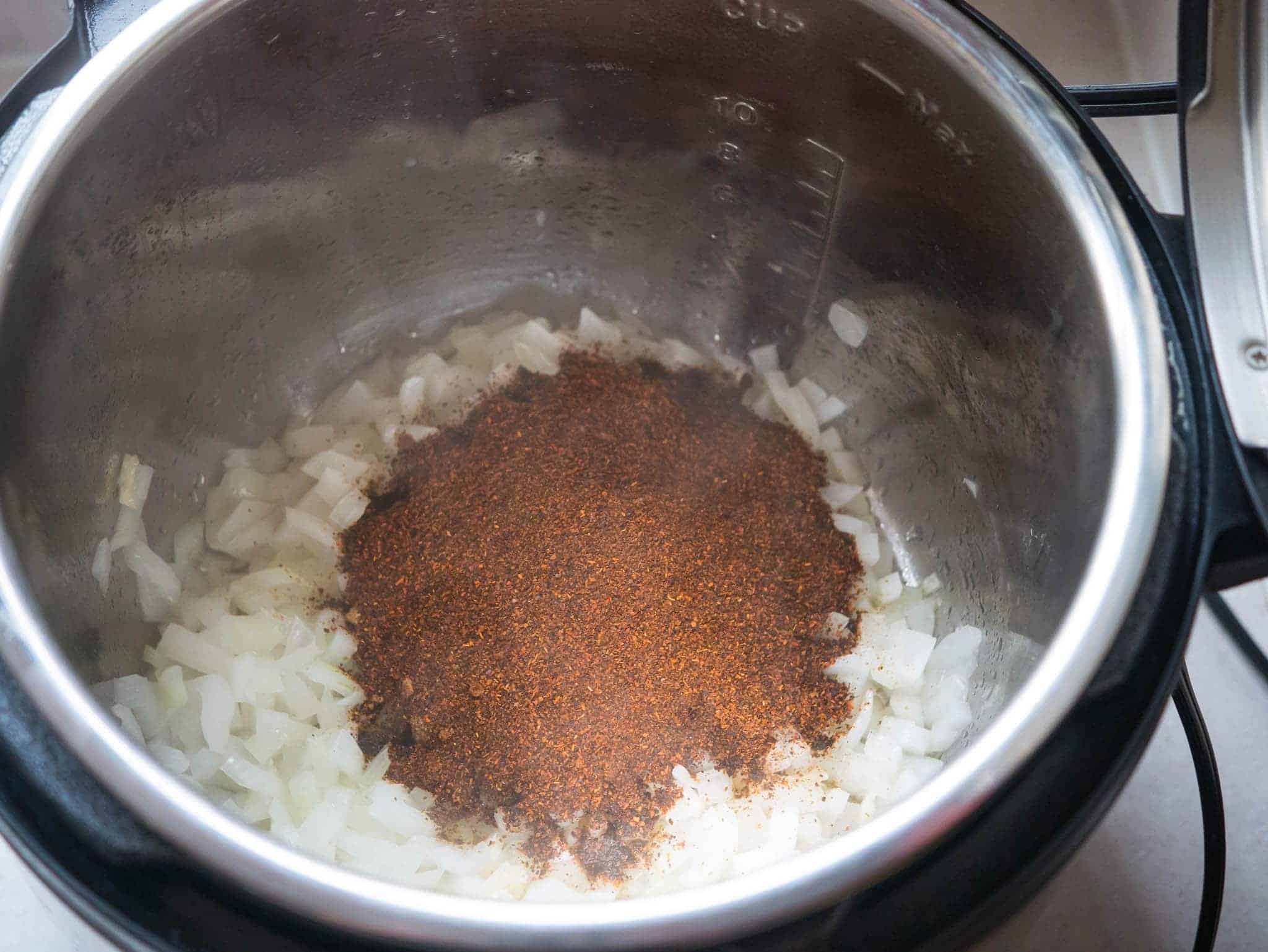 An Instant Pot full of sautéed onions, with dry spices on top