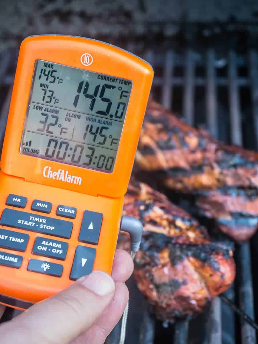 Thermometer showing 145°F and pork tenderloins on the grill