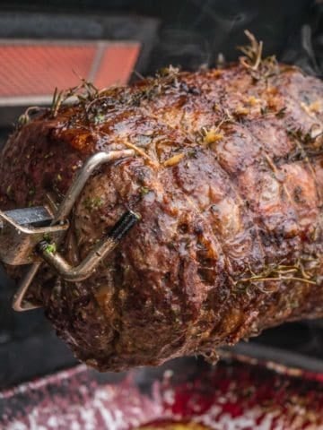 A boneless ribeye roast cooking on a gas grill rotisserie