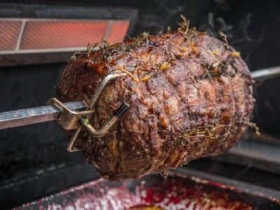 A boneless ribeye roast cooking on a gas grill rotisserie