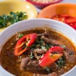 A bowl of panang curry topped with sliced basil and hot peppers, with crushed peanuts in the background