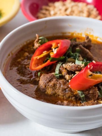 A bowl of panang curry topped with sliced basil and hot peppers